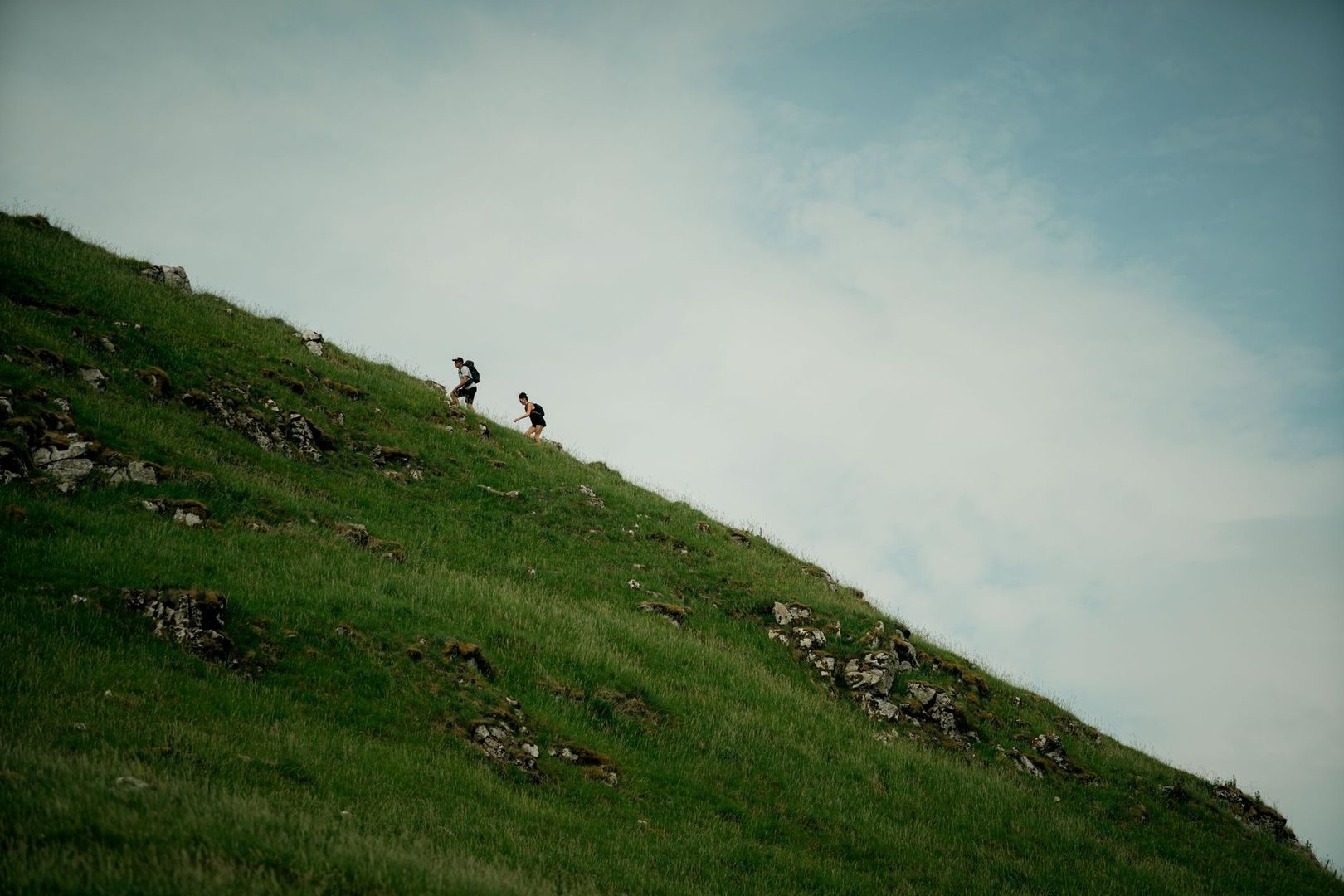 Zwei Trailrunner steigen einen steilen, grasbewachsenen Berghang hinauf